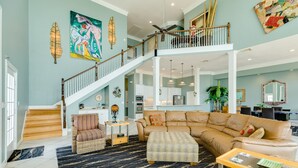 A spacious living area with a high ceiling, a staircase, and a large sofa. - 2nd row Gulf Views, Open Floor Plan, 2 Decks & Dog Friendly in Indian Beach (Galveston)