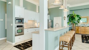 A modern kitchen with white cabinets, stainless steel appliances, a central island with stools, and pendant lighting. - 2nd row Gulf Views, Open Floor Plan, 2 Decks & Dog Friendly in Indian Beach (Galveston)