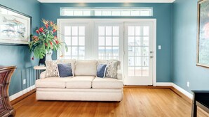 A living room with a beige sofa, a potted plant, and a framed picture on the wall. - 2nd row Gulf Views, Open Floor Plan, 2 Decks & Dog Friendly in Indian Beach (Galveston)