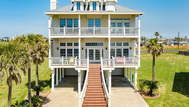 A two-story beachfront house with a central staircase, balconies, and palm trees. - 2nd row Gulf Views, Open Floor Plan, 2 Decks & Dog Friendly in Indian Beach (Galveston)
