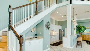 A spacious kitchen with white cabinets, a wooden staircase, and a dining area with a chair and table. - 2nd row Gulf Views, Open Floor Plan, 2 Decks & Dog Friendly in Indian Beach (Galveston)