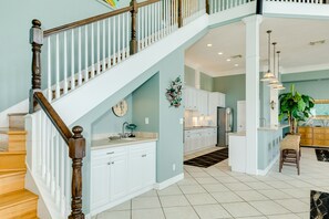 A spacious kitchen with white cabinets, a wooden staircase, and a dining area with a chair and table. - 2nd row Gulf Views, Open Floor Plan, 2 Decks & Dog Friendly in Indian Beach (Galveston)
