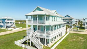 Et fleretagers hus ved stranden med balkon, trappe og indhegnet gård.