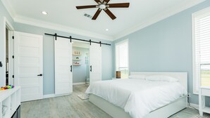 Et soveværelse med en stor seng, ventilator i loftet og en skydedør til et badeværelse.
