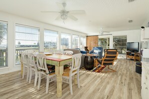 Relax in this stylish room with a dining table, sofa, and TV, surrounded by large windows and a wooden floor.