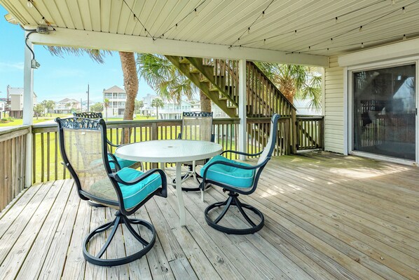 A covered outdoor area with a table and chairs, a wooden deck, and a view of buildings in the background.