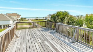 Eine Holzterrasse mit Geländer, die auf einen Strand und das Meer blickt.