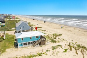 Une maison de plage avec un toit en métal, une véranda et un escalier menant à une terrasse.