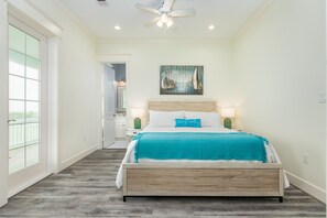 A bedroom with a bed, a ceiling fan, a painting, and a view through a window. - Beachside Home w/ Gulf Views Built 2019, 3 Decks, Pointe West Resort Amenities (Galveston)