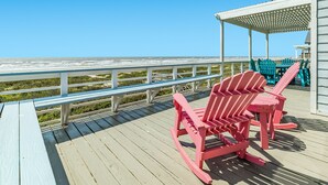Een houten terras met uitzicht op de oceaan, een overdekt gedeelte met stoelen en een reling.