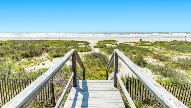 Een houten looppad dat naar een strand leidt, onder een heldere lucht.
