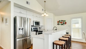 A modern kitchen with stainless steel appliances, white cabinetry, and a central island with bar stools. - Updated Beachfront Home w/ Elevator+Ramp, 2 Primary Suites, Great Gulf Views (Galveston)