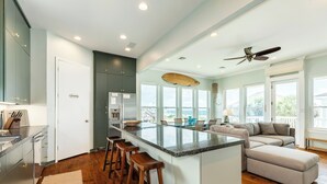 A spacious kitchen with a large island, bar stools, and a view of the ocean through large windows. - Bright & Airy 3rd Row Home w/ Gulf Views, 2 Decks, Outdoor Shower, Free Wifi (Galveston)
