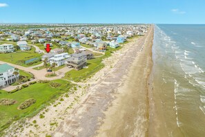 Vue aérienne d’une zone résidentielle côtière, avec des maisons, une plage et un ciel dégagé.