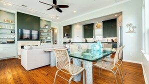 A modern kitchen with dark cabinets, a glass dining table, wicker chairs, and a ceiling fan. - Bright & Airy 3rd Row Home w/ Gulf Views, 2 Decks, Outdoor Shower, Free Wifi (Galveston)