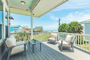 A covered deck with outdoor furniture, a view of the ocean, and neighboring houses.