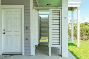 Une maison avec une porte blanche, un porche abrité et un escalier apparent menant à l’étage supérieur.