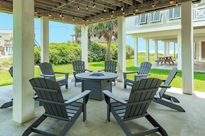 Un espace extérieur aménagé, abrité et doté de chaises Adirondack et d’une table ronde, offrant une vue sur une pelouse et un bâtiment doté d’un balcon.