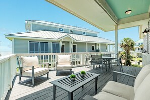 A covered outdoor deck with seating, a table, and a view of a large house.