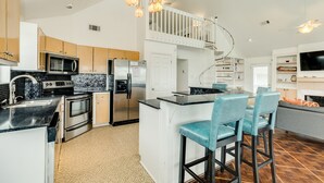 Una cocina moderna con electrodomésticos de acero inoxidable, una isla central con taburetes y una escalera que sube a un nivel superior.