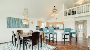 Una cocina moderna con una isla central, taburetes de bar y un comedor con alfombra estampada y sillas.