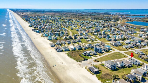 Vista aérea de una zona residencial costera con casas a lo largo de la playa y una gran masa de agua al fondo.