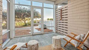 Un patio spacieux avec une porte-fenêtre coulissante donnant sur un jardin, des chaises longues en bois et un élément décoratif fixé au mur.