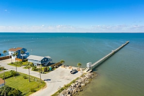 A coastal property with a long pier extending into the water, a parking area, and a house with a blue roof. - Updated Beachfront Home w/ Gulf Views, 2 Decks, Free Wifi, Open Layout (Galveston)