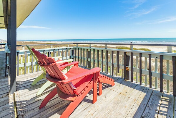 A wooden deck with a red Adirondack chair overlooking a beach. - Updated Beachfront Home w/ Gulf Views, 2 Decks, Free Wifi, Open Layout (Galveston)