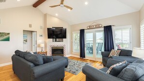 Ein Wohnzimmer mit grauen Sofas, einem Flachbildfernseher, einem Kamin und einem Schild mit der Aufschrift 'BEACH HOUSE'.