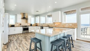 Een moderne keuken met witte kasten, een groot eiland met krukken en uitzicht op buiten.