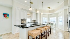 A spacious kitchen with white cabinetry, a black countertop, and a central island with bar stools.