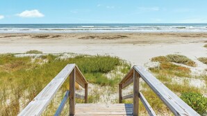 A wooden boardwalk leading to a beach with sand and grass.