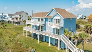 A two-story beachfront house with a balcony and a staircase leading to the upper level.