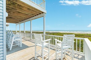 Une terrasse en bois, dotée de rampes et de chaises blanches, qui offre une vue sur la plage.