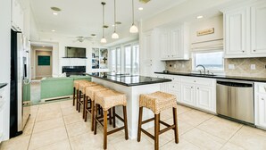 A kitchen with white cabinets, a central island with bar stools, a dishwasher, and pendant lighting.