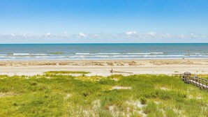 Een strand met een houten promenade die naar het water leidt, begroeide duinen en een heldere lucht.