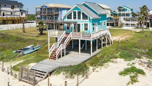 A beachfront house with a wooden deck, a staircase, and a view of the ocean. - Cozy Beachfront, Pet Friendly Home w/ Loft & Covered Patio - Steps from Beach! (Galveston)