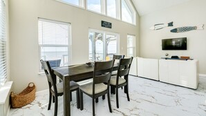 A dining area with a wooden table and chairs, a white cabinet, and a TV mounted on the wall. - Cozy Beachfront, Pet Friendly Home w/ Loft & Covered Patio - Steps from Beach! (Galveston)