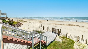 A beach with a wooden boardwalk leading to a beach hut, a clear sky, and the ocean in the background. - Cozy Beachfront, Pet Friendly Home w/ Loft & Covered Patio - Steps from Beach! (Galveston)