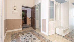 A hallway with patterned floor tiles, a white door with a glass panel, and a small white bench.