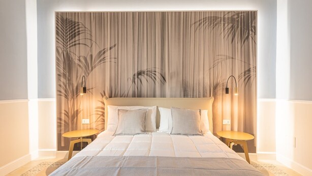 A neatly made bed with a headboard, two bedside tables, and a wall with a vertical plant pattern.