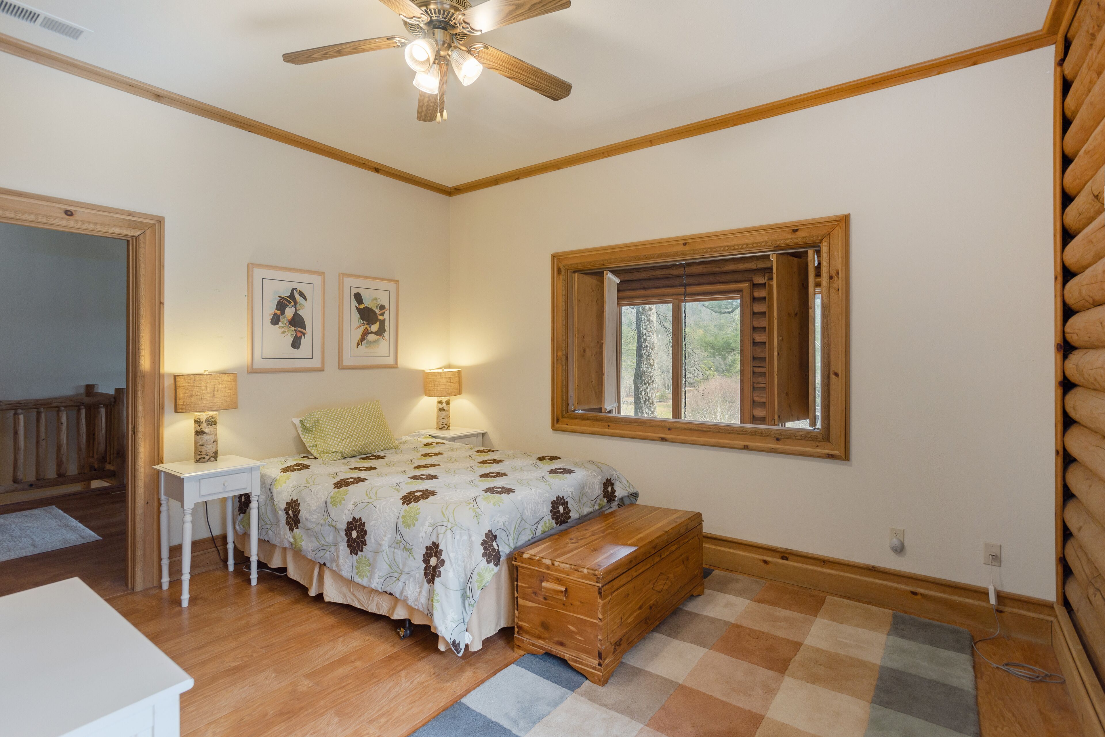 A bedroom with a bed, bedside lamps, a wooden chest, a window, and a ceiling fan.