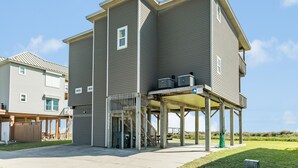 A two-story building with a covered outdoor area and a visible staircase leading to the upper floor. - Elevator, 2 Decks, Gulf Views all Bedrooms & More - Private Beachfront Home (Galveston)