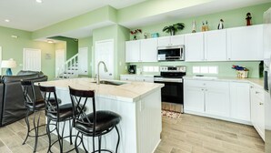 A modern kitchen with white cabinets, a central island with bar stools, and a staircase leading to another level. - Elevator, 2 Decks, Gulf Views all Bedrooms & More - Private Beachfront Home (Galveston)