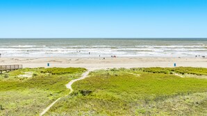 Una playa con un paseo de madera que conduce al agua, arena y dunas de hierba en primer plano.