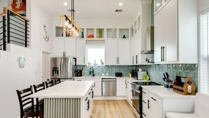Una cocina moderna con armarios blancos, una isla central y un comedor con sillas.