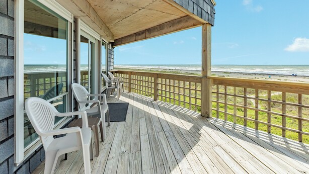 Una terraza de madera con barandilla, con vista a una playa.