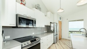 Una cocina moderna con electrodomésticos de acero inoxidable, armarios blancos y un amplio ventanal con vistas al océano.
