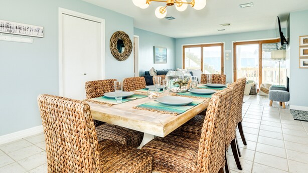 A dining area with a wooden table set for six, surrounded by wicker chairs. - Willy's Place: 3rd Row Gulf View Home with Updated Interior & Rooftop Sun Deck (Galveston)